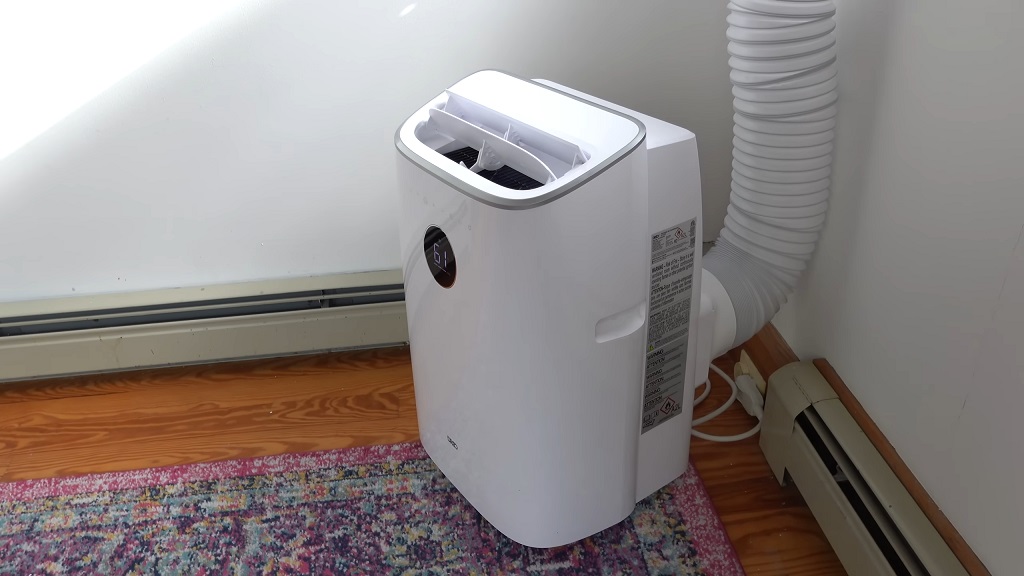 Prenosna klima postavljena na drveni pod pored zida